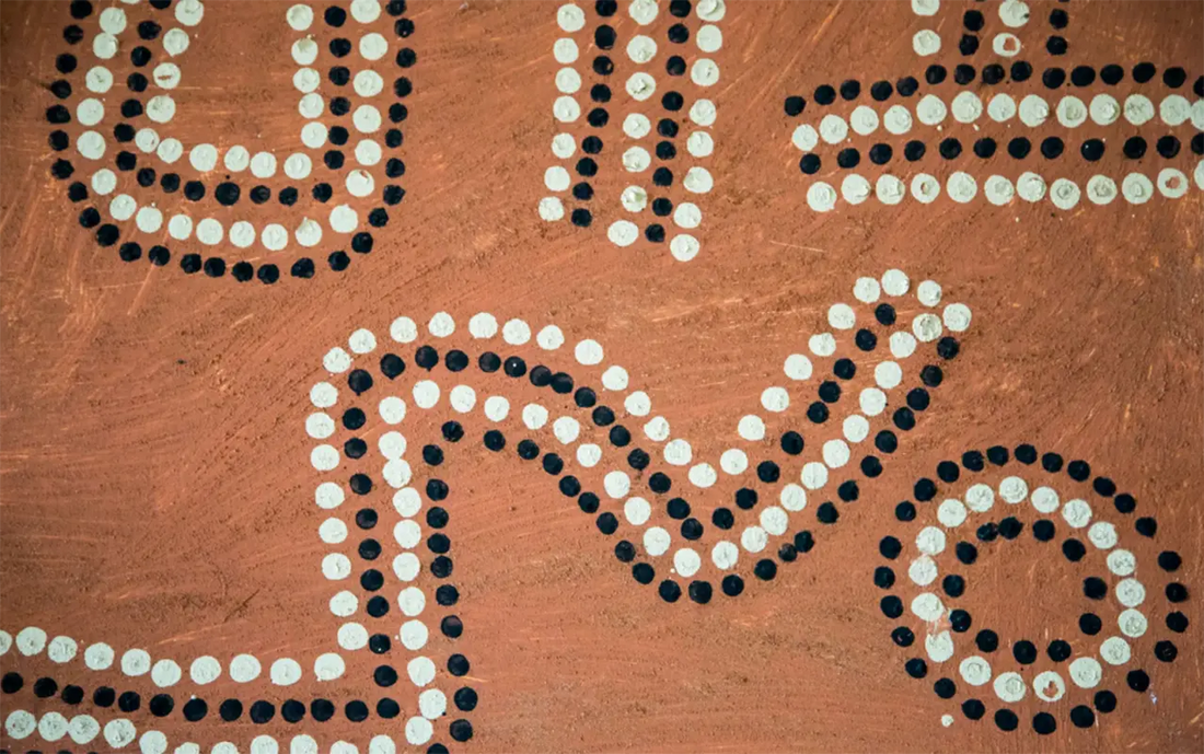 Close-up of Aboriginal dot painting on ochre-red background, showing black-and-white dotted lines forming winding, U-shaped, and spiral patterns.