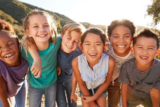 Six happy children laughing and playing outdoors in sunshine, enjoying screen-free time together in nature.