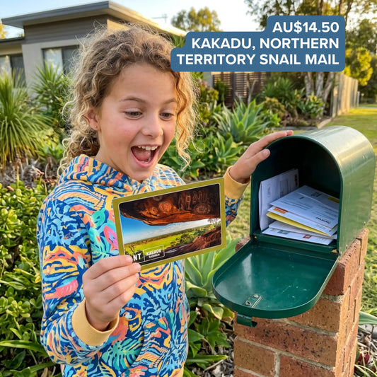 Child excitedly holding a Kakadu, Northern Territory postcard featuring Aboriginal rock art beside an open mailbox full of Snail Mail envelopes.