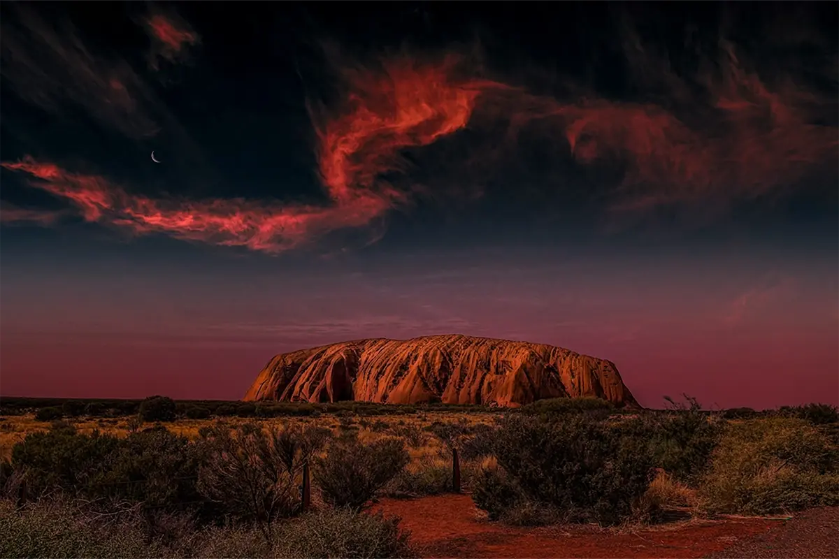 Uluru rising from the Australian desert under a dramatic night sky, representing the deep connection to Country celebrated in True Blue Pen Pals