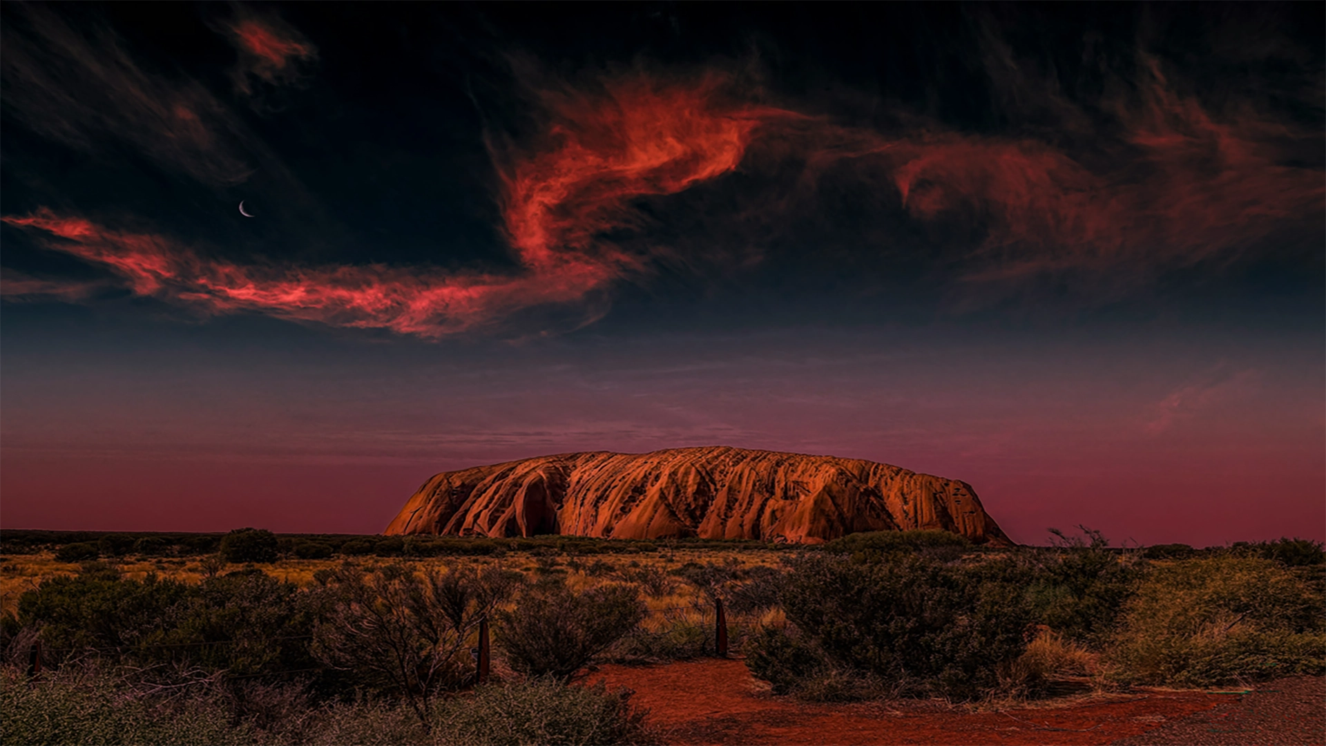 Uluru rising from the Australian desert under a dramatic night sky, representing the deep connection to Country celebrated in True Blue Pen Pals