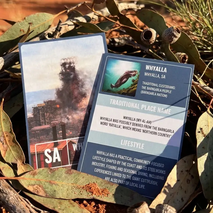True Blue Pen Pals Whyalla collector cards styled on red dirt with eucalyptus leaves — front shows steelworks image, back features Giant Cuttlefish, Barngarla traditional place name and lifestyle facts
